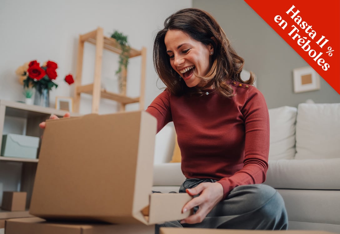 mujer abriendo paquete en el salón de su casa con cara de felicidad.