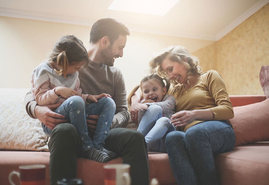 familia con niñas pequeñas riendo en el sofá