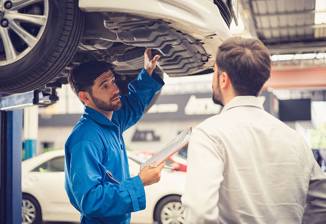 Mecánico atendiendo a conductor en el taller mientras hace la revisión del coche