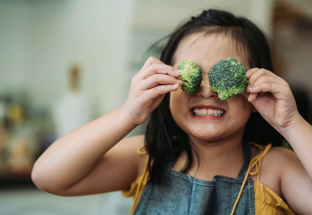 niña jugando con brócoli como si fuesen gafas