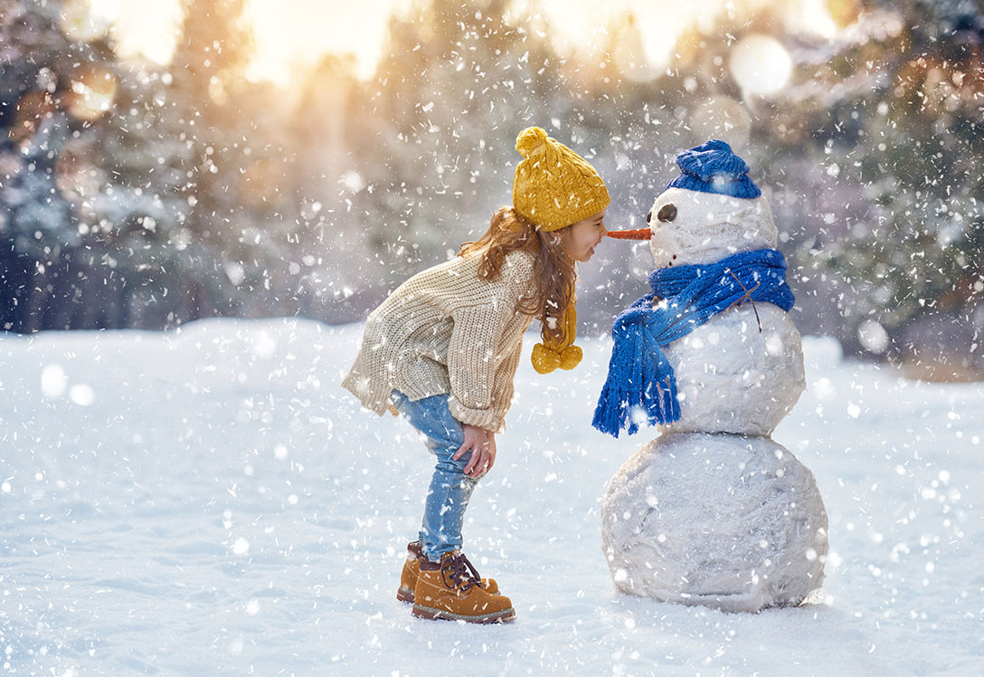 niña y muñeco de nieve en paisaje invernal