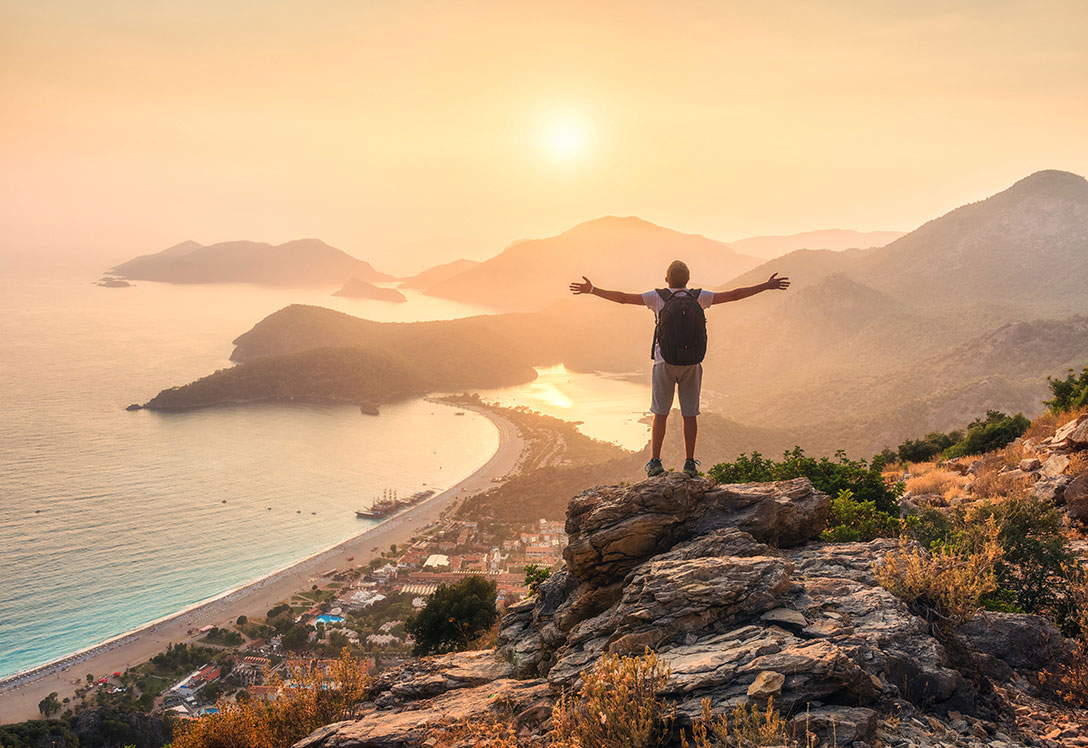 Hombre sobre la montaña con brazos abiertos observando la playa al atardecer