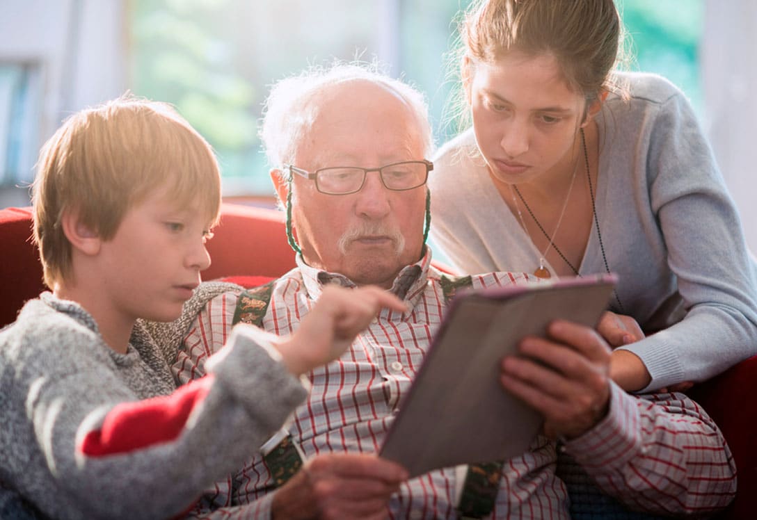 Un abuelo revisa la tablet ayudado por sus nietos