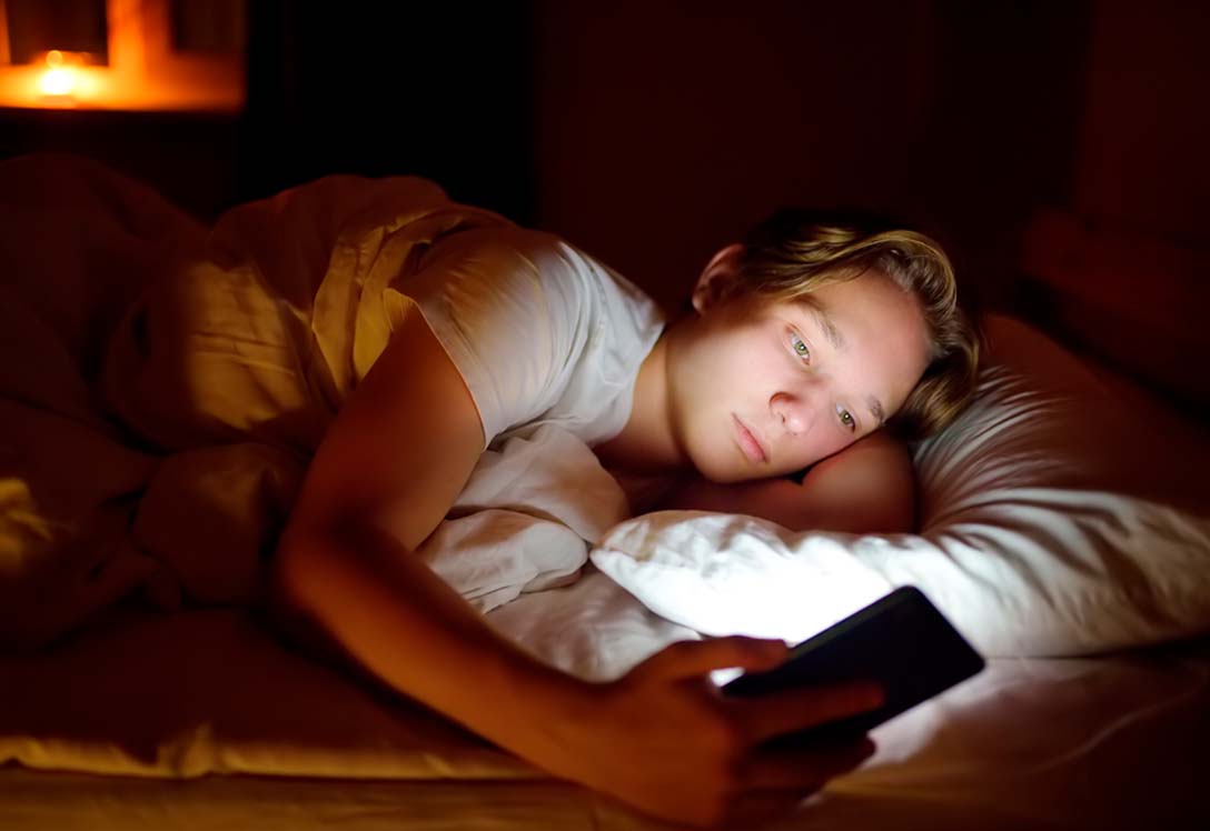 Adolescente consulta el móvil en la cama