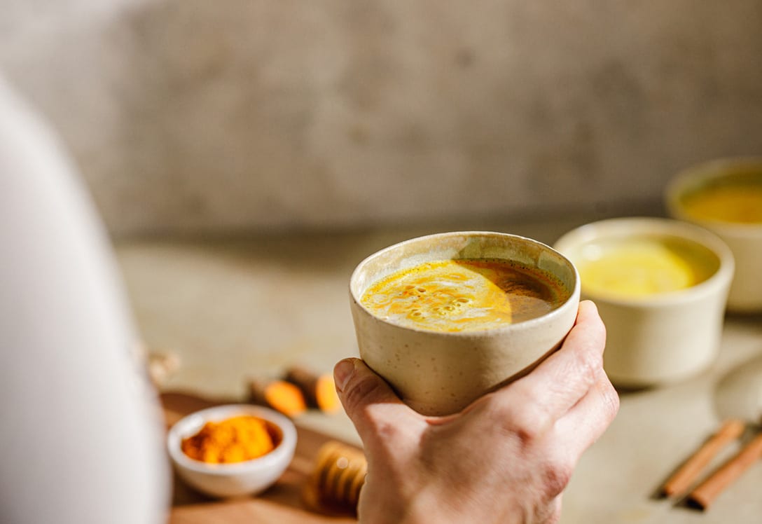 curcuma-cafe-beneficios mano que sostiene un café que lleva cúrcuma