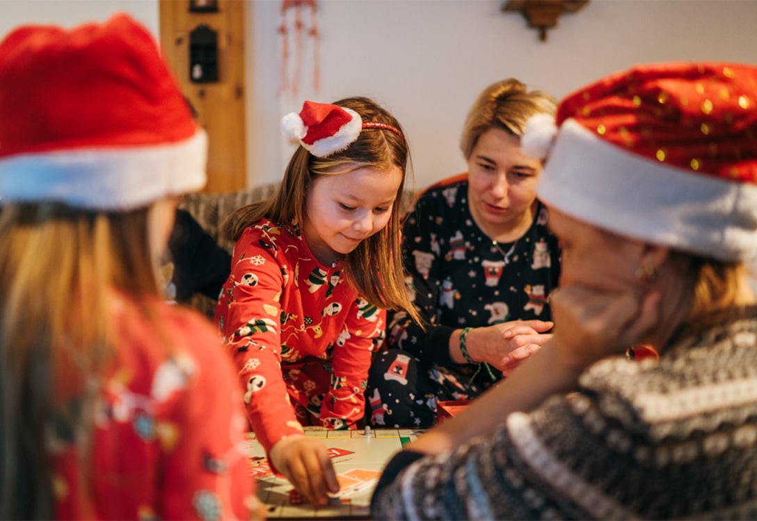 niña jugando juegos de mesa con su familia en navidad con gorritos de papanoel puestos