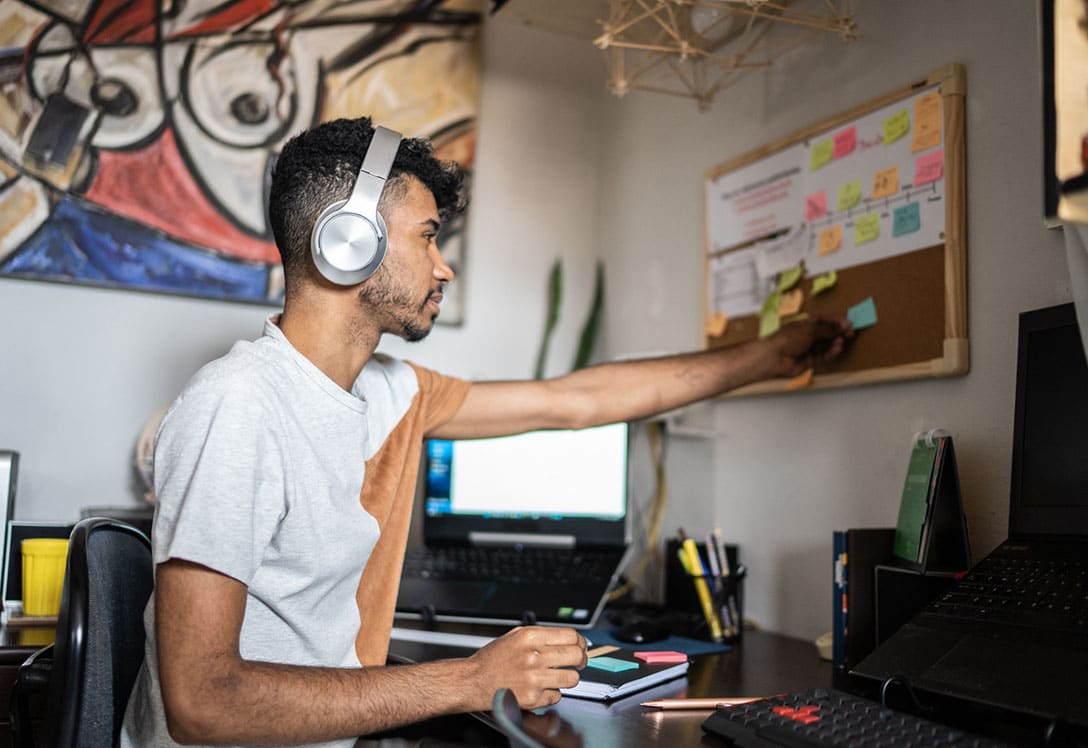 joven-planificando-tiempo-estudio chico con cascos planificando tiempo de estudio en un tablero de corcho sobre su mesa de estudio
