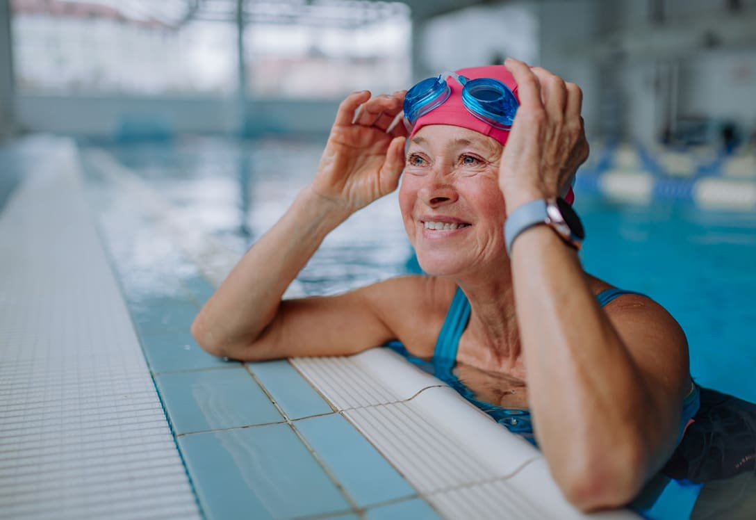 mujer senior dentro de la piscina, sonrie y se levanta las gafas de buceo en su clase de natación