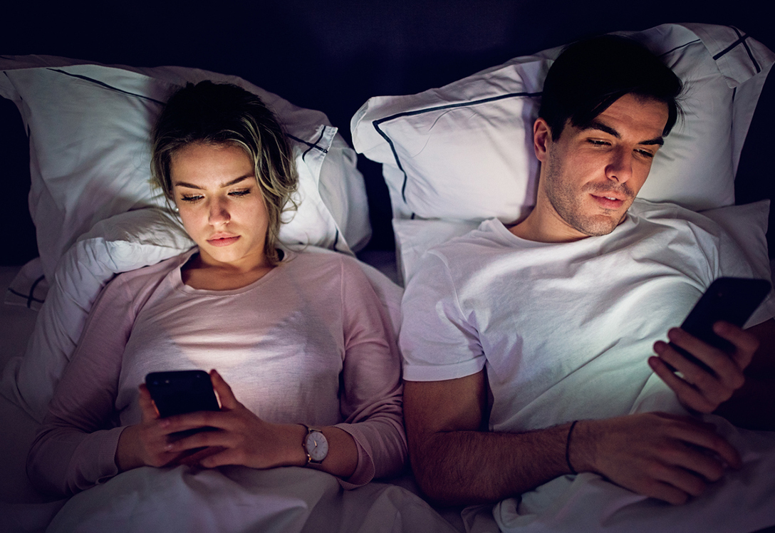 pareja en la cama a la hora de dormir mirando pantallas de sus móviles