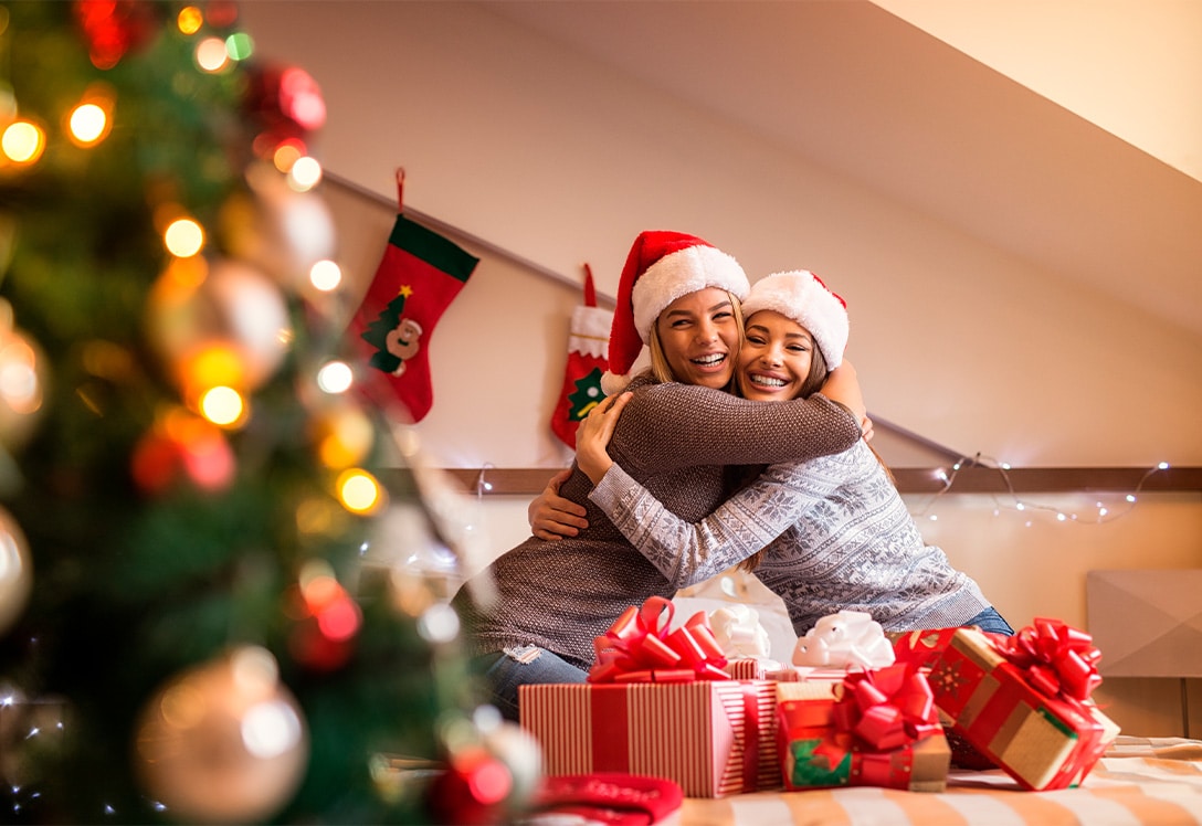 amigas abrazadas celebrando navidad frente a los regalos y el arbol de navidad